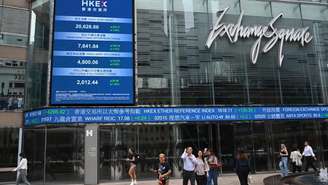 Pessoas passam sob painel eletrônico com índices da Bolsa de Valores de Hong Kong, em 10/4/25.