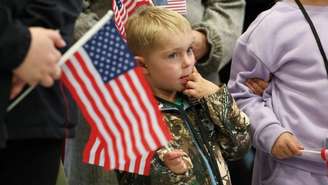 Integrantes do primeiro grupo de sul-africanos brancos que receberam o status de refugiados nos EUA segurando bandeiras dos EUA enquanto participam de um evento de boas-vindas no Aeroporto Internacional de Dulles