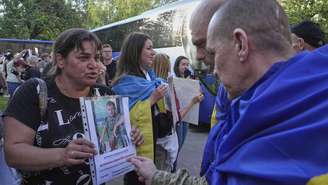 Pessoas mostram fotos de seus parentes a prisioneiros de guerra ucranianos quando eles chegam do cativeiro durante uma troca de prisioneiros entre a Rússia e a Ucrânia, na região de Chernyhiv, Ucrânia, sexta-feira, 23 de maio de 2025.