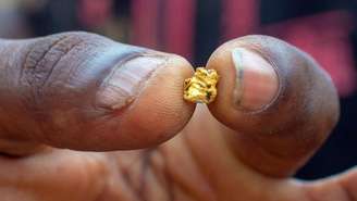 Pepita de ouro entre o polegar e o indicador de um mineiro ilegal no oeste da África