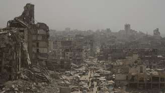 Pessoas caminham por uma rua ladeada por prédios destruídos após bombardeios israelenses durante a guerra entre Israel e o Hamas na Faixa de Gaza, terça-feira, 29 de julho de 2025.