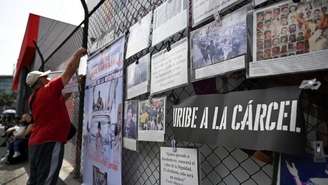 Um homem pendura cartazes em uma grade pedindo a prisão do ex-presidente colombiano Álvaro Uribe durante seu julgamento em frente ao Complexo Judicial de Paloquemao, em Bogotá, em 28 de julho de 2025.