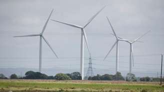 Turbinas eólicas terrestres no Parque Eólico Little Cheyne Court operam ao lado de torres de eletricidade em Dungeness, Grã-Bretanha, em 10 de julho de 2024. Ilustração.