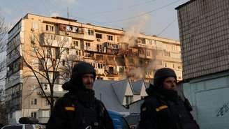 Equipes de emergência ucranianas caminham em frente a um prédio residencial danificado após um ataque aéreo em Kiev, em 14 de novembro de 2025, em meio à invasão russa da Ucrânia.