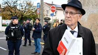 Jacques Boncompain (à direita), presidente da ADMP (Associação para Defender a Memória do Marechal Pétain), segura um livro que escreveu após um protesto em frente à igreja Saint-Jean-Baptiste, onde ocorreu uma cerimônia religiosa “em homenagem ao marechal Pétain e seus soldados”, organizada pela ADMP em Verdun, nordeste da França, em 15 de novembro de 2025.