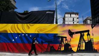 Um homem usando uma máscara e passando em frente a um mural com uma máquina de extração de óleo e a bandeira da Venezuela