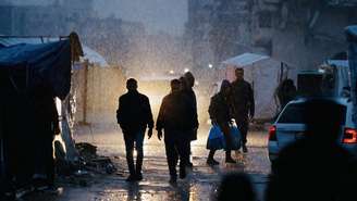 Palestinos deslocados caminham na chuva na Cidade de Gaza em 15 de dezembro de 2025. O cessar-fogo patrocinado pelos EUA, em vigor desde 10 de outubro, interrompeu a guerra que começou após o ataque mortal do Hamas contra Israel em 7 de outubro de 2023. Mas permanece frágil, já que Israel e o Hamas se acusam mutuamente de violações quase diariamente.