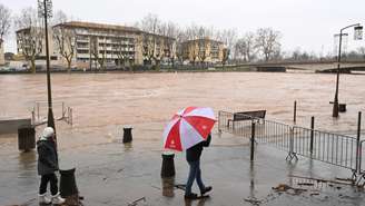 Um pedestre com um guarda-chuva caminha pelas ruas alagadas de Agde, no sul da França, tirando uma foto após o rio Hérault transbordar devido às fortes chuvas, em 23 de dezembro de 2025.