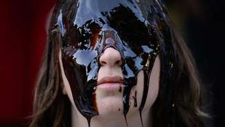 Uma mulher com o rosto coberto por uma substância oleosa.