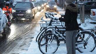 Uma mulher segura uma bicicleta ao lado de carros em uma rua durante uma nevasca em Paris, em 5 de janeiro de 2026.