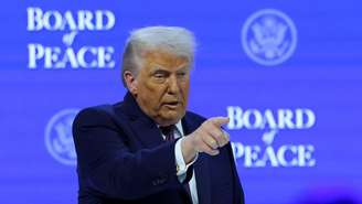 Donald Trump apontando para a plateia, sobre um fundo azul alusivo ao Conselho de Paz criado por ele
