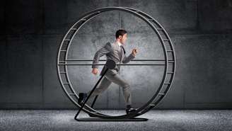 Homem de terno e gravata correndo em uma roda de hamster gigante