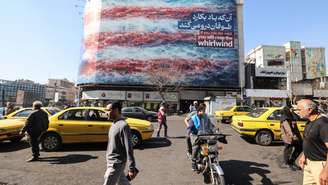 Iranianos passam por um outdoor anti-EUA instalado em um prédio na Praça Enqelab, em Teerã, em 17 de fevereiro de 2026.