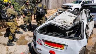 Forças de segurança israelenses e equipes de resgate perto de um veículo destruído no local de um ataque iraniano que atingiu um bairro residencial em Bat Yam, ao sul de Tel Aviv, em 9 de março de 2026.