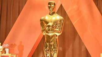 Estatueta dourada em frente à fundo neutro em tons bege de um palco  