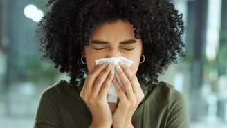 Uma mulher segurando um lenço no nariz enquanto espirra