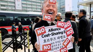 Ativista com máscara de Trump protesta contra envio de tropas ao Estreito de Ormuz, em frente à embaixada dos EUA em Seul. 16 de março de 2026