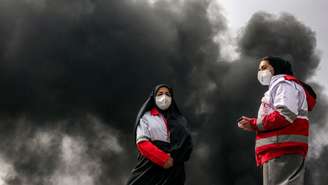 Funcionárias do Crescente Vermelho trabalham em meio a fumaça negra gerada após explosão de reservatório de petróleo em no noroeste de Teerã. (10/03/2026)