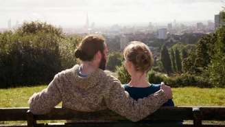 Um casal sentado em um banco de costas para a foto