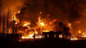 Grande incêndio em um depósito de petróleo no Irã à noite. Chamas e colunas de fumaça escura sobem sobre uma pequena construção