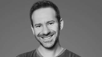 Retrato em preto e branco de Leonid Radvinsky, sorrindo e com barba por fazer e bigode.