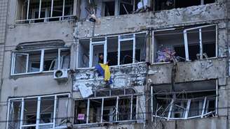 Um morador pendura a bandeira nacional ucraniana em sua varanda em um prédio de apartamentos atingido por um drone russo, em meio ao ataque da Rússia à Ucrânia, em Lviv, Ucrânia, em 24 de março de 2026.