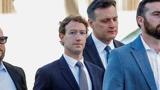 Mark Zuckerberg cercado por três seguranças enquanto caminha em direção a um tribunal de Los Angeles, vestindo um blazer azul-marinho, gravata cinza e camisa branca.