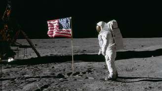O astronauta Edwin E. Aldrin Jr., piloto do módulo lunar da primeira missão de pouso na Lua, posa para uma fotografia ao lado da bandeira dos Estados Unidos hasteada durante uma atividade extraveicular (EVA) da Apollo 11 na superfície lunar.