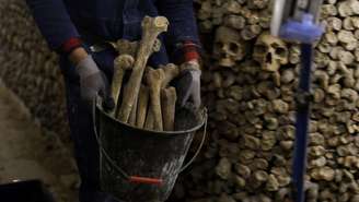 Um operário transporta ossos humanos em um balde dentro das Catacumbas de Paris, em 24 de março de 2026, durante obras de restauração do monumento parisiense.