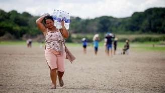 Mulher carrega garrafões de água em terreno árido no Brasil durante uma onda de calor