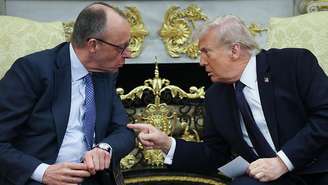 Trump e Merz conversam no Salão Oval. Eles estão sentados e inclinados um em direção ao outro. Trump aponta o dedo para Merz.