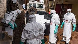 Funcionários da Sociedade da Cruz Vermelha de Uganda são borrifados com desinfetante durante a remoção do corpo de uma suposta vítima de ebola em Kampala, em 26 de maio de 2026.