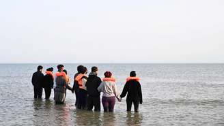 Grupo de migrantes caminham pela água para embarcar em um bote no norte da França para tentar atravessar o Canal da Mancha, em 23 de maio de 2026.