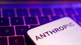 Uma tela de smartphone mostrando o logotipo da Anthropic em letras pretas em um fundo todo branco, colocado em um teclado de laptop iluminado em rosa e roxo