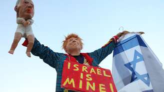 Ativista israelense de esquerda, fantasiado de Donald Trump, segura fantoche de bebê representando Benjamin Netanyahu durante manifestação contra a guerra no Oriente Médio.
