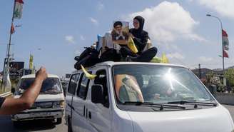 Libanesa deslocada segura cartaz do falecido líder do Hezbollah, Hassan Nasrallah, enquanto volta para casa com familiares no sul do Líbano.