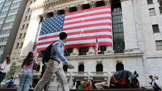 A Bolsa de Valores de Nova York, nos Estados Unidos, em manhã de negócios no dia 26 de maio de 2026, com uma grande bandeira americana na frente do edifício e pessoas andando na calçada