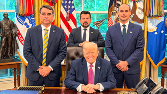Flavio Bolsonaro, Paulo Figueiredo e Eduardo Bolsonaro de pé, em volta de Trump, que está sentado, em sua mesa no Salão Oval