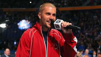 Justin Bieber veste uma jaqueta vermelha e segura um microfone com o logotipo da NHL enquanto participa do Draft da NHL de 2026, em 26 de junho de 2026, em Buffalo, Nova York.
