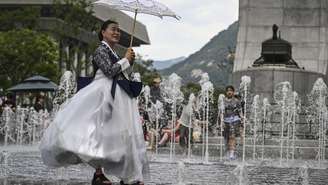 Uma mulher vestida com um Hanbok tradicional posa para uma foto na Praça Gwanghwamun, em meio à onda de calor, em Seul, em 12 de julho de 2026.