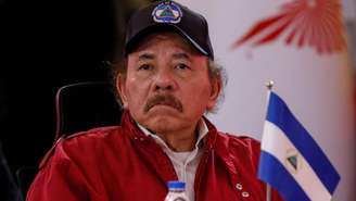 Daniel Ortega, de boné e jaqueta vermelha, ao lado de uma pequena bandeira da Nicarágua