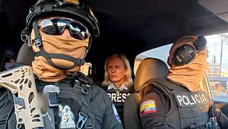 Dois policiais equatorianos com óculos de sol, capacetes e balaclavas, sentados em um carro com a jornalista da BBC Orla Guerin na parte de trás, vestindo uma jaqueta com a palavra 'IMPRENSA' em inglês