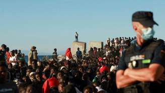 Migrantes aguardam na fila para receber alimentos e bebidas da Cruz Vermelha, após travessias em massa a pé e por via marítima do Marrocos para o enclave espanhol de Ceuta. 3 de agosto de 2026