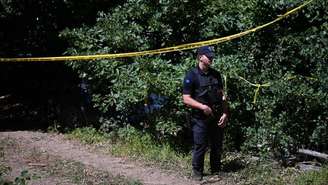 Um policial do Kosovo monta guarda na área isolada perto de uma vala comum recentemente descoberta na vila de Kalluder, próxima à cidade de Zubin Potok, em 1º de agosto de 2026.