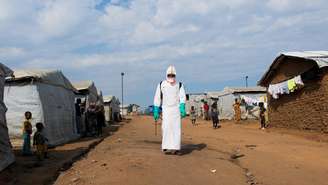 Moradores observam agente de saúde desinfetar a área no campo de deslocados em Bunia, no leste da RDC, em 18 de junho de 2026.