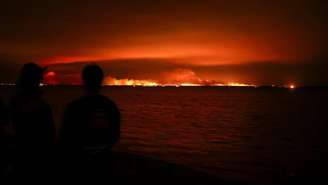 Turistas observam incêndio florestal atingir uma área de mata próxima à baía de Arcachon, no oeste da França, em meio ao agravamento da seca após uma onda de calor e à escassez de água em grande parte do país, em 24 de julho de 2026.