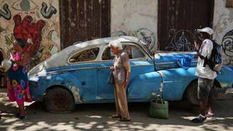 Imagem de arquivo. Pessoas passam por um carro com pneu furado em Havana Velha, Cuba, em 6 de janeiro de 2026. País sofre com aceleração de crise demográfica.