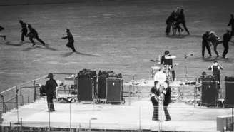 Policiais retiram os fãs eufóricos do campo enquanto os Beatles se apresentam em um palco no Candlestick Park, em San Francisco, Califórnia