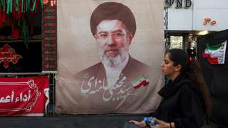 Uma mulher caminha ao lado de um cartaz com a imagem do líder supremo do Irã, Mojtaba Khamenei, em uma rua de Teerã, Irã, em 13 de agosto de 2026.
