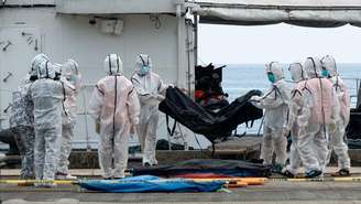 Uma equipe da Guarda Costeira das Filipinas, usando trajes de proteção, descarrega sacos mortuários com vítimas do incêndio em um ferry no porto de Borac, em Coron, na província de Palawan, em 12 de setembro de 2026.